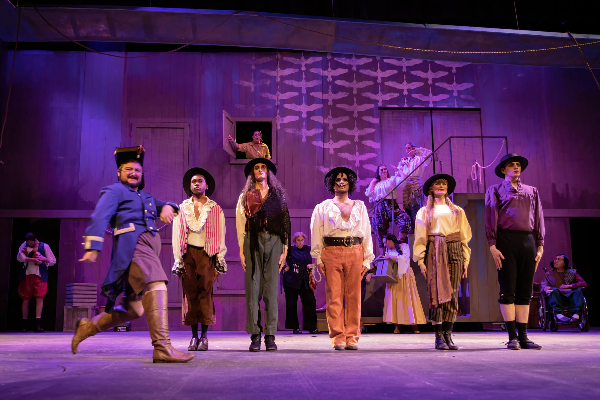 Pirates stand in a line downstage while an ensemble occupies joke wall doors and the slide stairs.